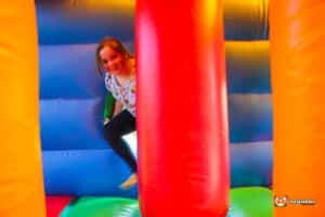 A girl plays energetically in 'The Colossal' inflatable bouncy castle, with colorful structures and a cheerful atmosphere.