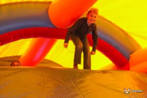 A boy happily slides down inflatable slide, illustrating a moment of fun and adventure in an outdoor play area.
