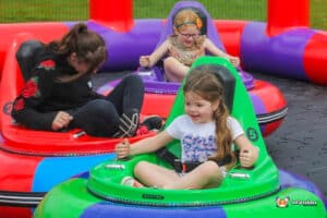 Three children laughing as they ride a bumper car in a lively inflatable play area.