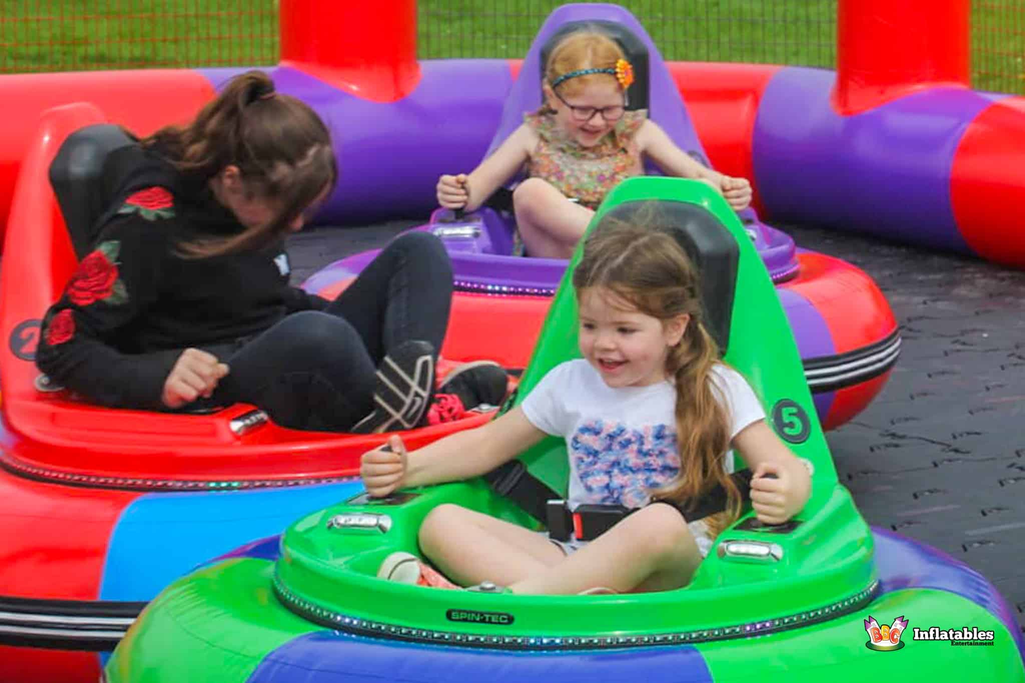 Three children laughing as they ride a bumper car in a lively inflatable play area.
