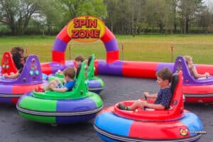 Children happily ride a bumper car in a colorful inflatable amusement setup.