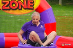 A man seated on a purple inflatable bumper car, smiling as he enjoys the ride.