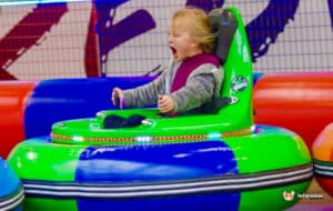 A young child joyfully rides an inflatable bumper car, smiling as they navigate a colorful play area.
