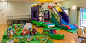 Indoor children's play area with inflatable structures featuring animal designs, a slide, and ride-on toys on a hardwood floor.
