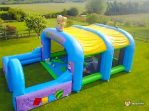 A soft play inflatable arena featuring a teddy bear perched on top, inviting children to play and explore.