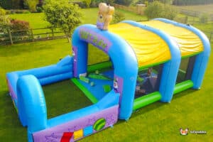 A colorful soft play inflatable arena with a teddy bear on top, designed for children's fun and safe play.