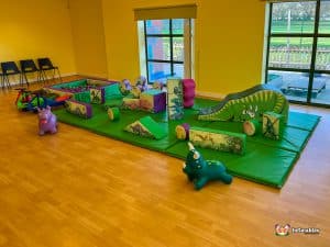 Dinosaur party soft play shapes on green mats with ball pool.