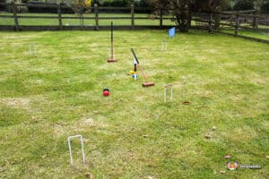 A grassy yard with croquet equipment set up, including balls, mallets, and hoops, ready for a game on a sunny day.