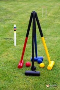 Colorful croquet mallets and balls arranged on green grass, with white and red goal posts in the background. Fun outdoor game setup.