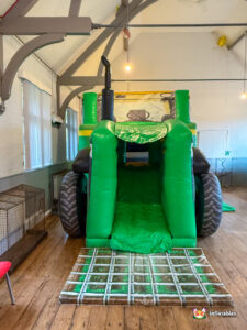 Rear view of the inflatable tractor, showing the green slide exit ramp that drops onto a mat designed to look like a plowed brown and green field.