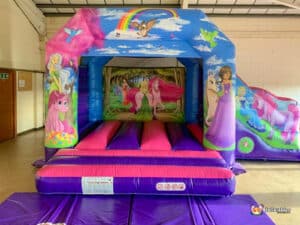 A lively unicorn bouncy castle showcasing princesses, complemented by a cheerful rainbow in the sky.