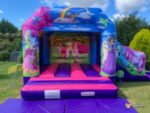 A whimsical unicorn bouncy castle adorned with princesses and a bright rainbow overhead.