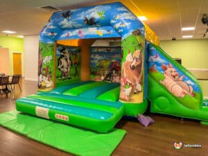 A cheerful farm-themed bouncy castle with a slide, providing a fun play area for children at outdoor gatherings.