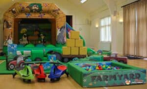 Children playing in a lively farmyard play area, complete with slides, climbing structures, and farm-themed decorations.
