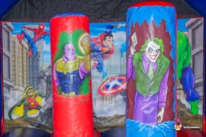A colorful bouncy castle featuring a large superhero theme, designed for children's entertainment at outdoor events.