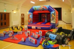 A superhero-themed inflatable bouncy castle, surrounded by toys, creating a fun and playful environment for children.