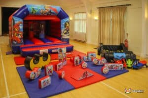 A vibrant inflatable bouncy castle adorned with superhero soft play toys, inviting children to jump and play.