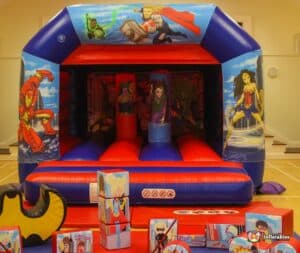 A large inflatable bouncy castle featuring superhero designs, surrounded by various toys and playful items for children.