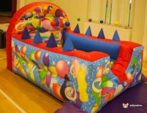 A lively bouncy castle containing a ball pool, surrounded by an assortment of balls on the floor.