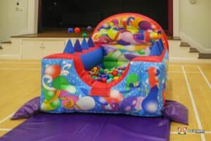 A vibrant bouncy castle featuring a ball pool, with numerous balls scattered across the floor.