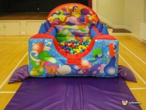 A colorful bouncy castle with a ball pool, filled with various balls scattered on the floor inside.