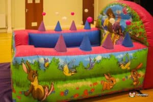 A princess castle play structure featuring princesses and a ball pool, set against a colorful backdrop.