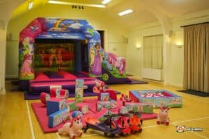 A colorful inflatable bounce castle with a fairy tale theme, surrounded by various playful toys and soft mats for children.