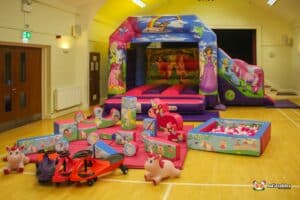 A colorful inflatable bouncy castle themed with unicorns and princesses, surrounded by playful toys and obstacles for children.
