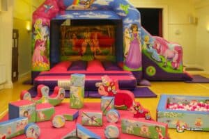 A colorful bouncy castle featuring magical themes, surrounded by playful blocks in a bright indoor party space.