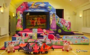 A colorful inflatable bounce house featuring unicorns and princesses, surrounded by soft play blocks and ride-on toys.