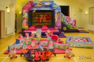 A colorful inflatable bounce house with cartoon characters, surrounded by play equipment including soft blocks and ride-on toys.