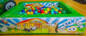 A large soft play area featuring a ball pit filled with colorful balls and various farm animal toys scattered around.