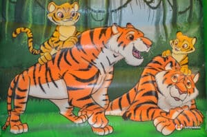 Four cartoon tigers, including two cubs, play together in a jungle setting, showcasing their vibrant orange and black stripes.