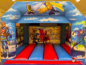 A colorful hero-themed bouncy castle in red and blue, equipped with plasma cars for children's entertainment.