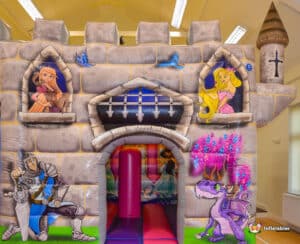 A bouncy castle styled as a medieval cabin, featuring a slide for kids to enjoy during outdoor festivities.