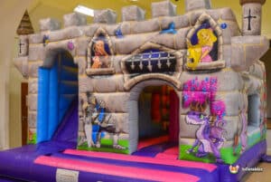 A colorful medieval cabin bouncy castle with an attached slide, ideal for children's entertainment at events.