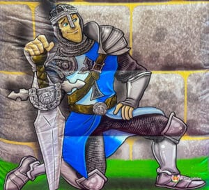 Cartoon character of a knight wielding a sword, playfully positioned on a bouncy castle, exuding fun and excitement.