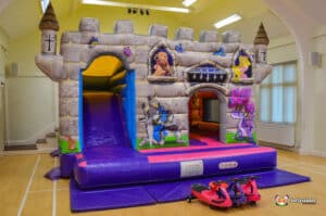 A colorful bouncy castle resembling a princess castle, equipped with a slide and plasma cars for children's entertainment.