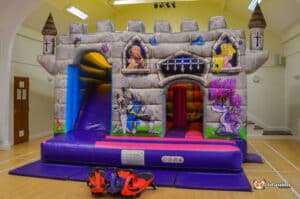 A playful medieval cabin bouncy castle with a slide, designed for children's enjoyment at parties and events.