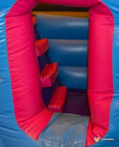 A blue and red inflatable bouncer featuring a slide, set up in a sunny outdoor area for children's play.