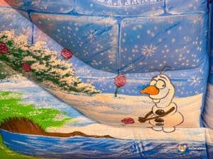 A snowman made of ice is positioned on a bouncy castle slide in a vibrant play area for children.