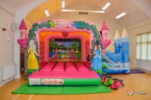 A colorful princess castle bouncy castle featuring a slide and turret, perfect for children's outdoor play.