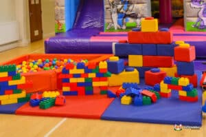 A children's play area with a slide, bouncy castle, large inflatable structures, and an assortment of building bricks.
