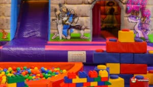 A cheerful play area featuring a slide, bouncy castle, inflatable structures, and scattered building bricks for creative play.