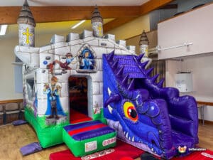 A colorful inflatable bounce castle shaped like a medieval fortress, featuring a dragon slide and playful illustrations on its walls.