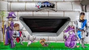A colorful inflatable castle with cartoon characters: a wizard, knight, dragon, and playful animals, set against a stone wall backdrop.