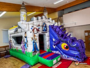 A colorful inflatable castle with a dragon, featuring cartoon characters and a vibrant design, set in a spacious indoor area.