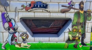A colorful inflatable castle scene features a knight, a dog in armor, and playful characters, set against a brick wall backdrop.