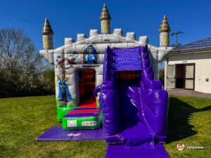A colorful inflatable castle with turrets and a slide, set in a grassy area under a clear blue sky.