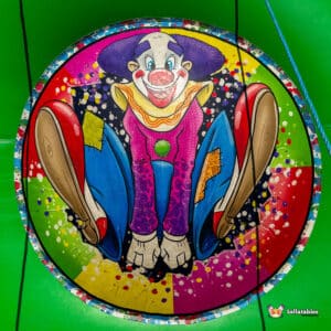 Colorful clown illustration with a big smile, sitting with outstretched legs, on a vibrant splatter-painted background.
